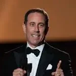 Clean comedian Jerry Seinfeld in a tux with microphone in hand