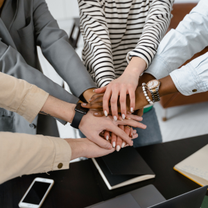 Picture of multiple people's hands on top of each other to promote hiring motivational speakers in Minnesota.