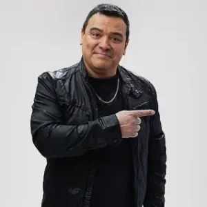 Celebrity comedian for hireCarlos Mencia in a black leather jacket pointing to the left with his left hand.