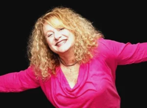 Female comedian and motivational speaker for hire Missy Hall in a pink blouse with her arms outstretched.